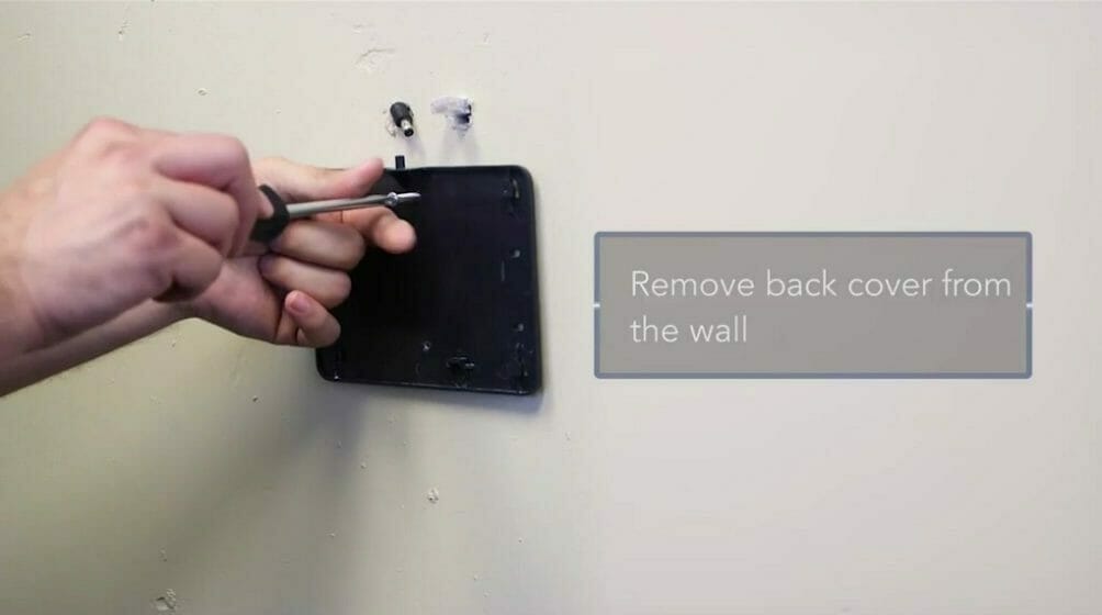 man removing the back cover of ADT from the wall using screw