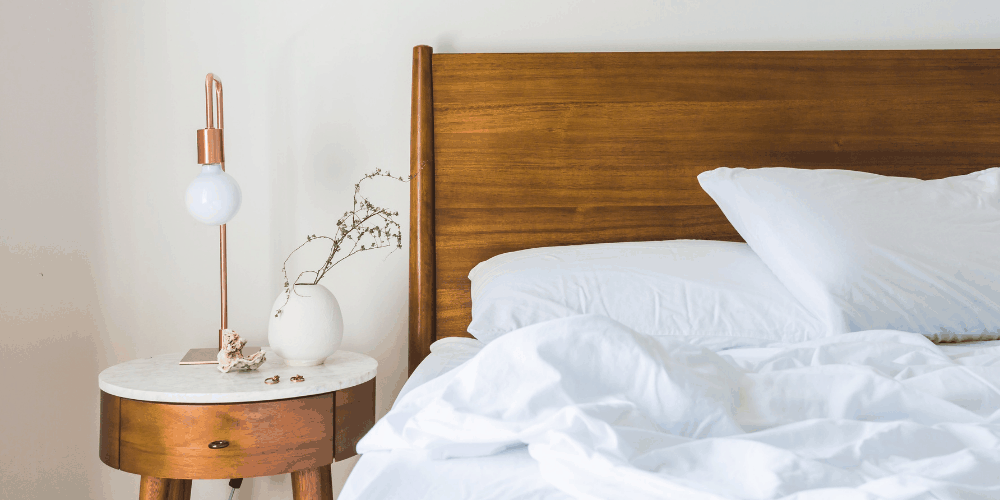 a nightstand and bed with white bedsheets and pilows
